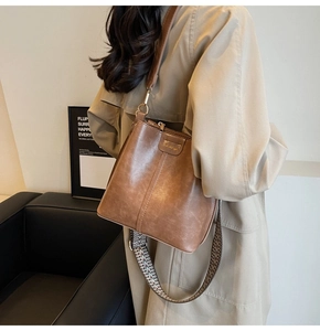 Détail du sac seau marron rétro en cuir avec une large bandoulière tissée géométrique