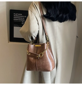 Detail of vintage brown bucket bag with gold chain and branded leather tag on a trench coat
