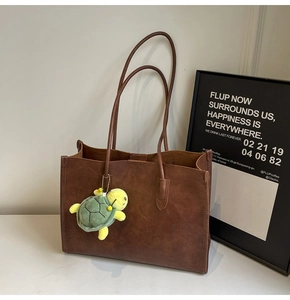 Dettaglio borsa tote in pelle marrone scuro con spalline lunghe e ciondolo a tartaruga