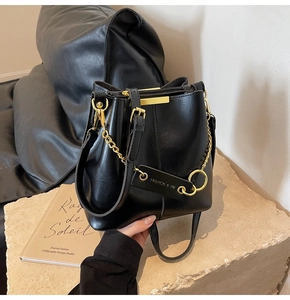 Detail of black leather bucket bag featuring gold chain strap and metallic hardware accents