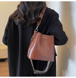 Brown leather bucket bag detail featuring a vintage woven wide strap and brand logo