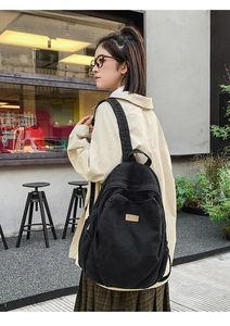 Detail view of durable black denim backpack showing side pocket and padded shoulder strap