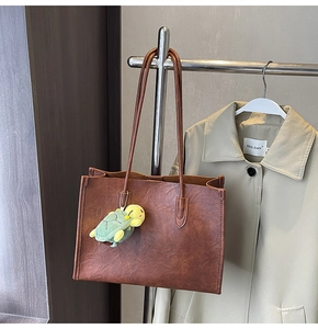 Dettaglio di una borsa tote in pelle marrone con un piccolo ciondolo a tartaruga