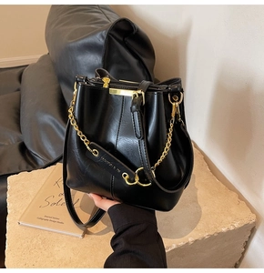 Detail of black glossy bucket bag featuring gold chain hardware and fashion embossed tag