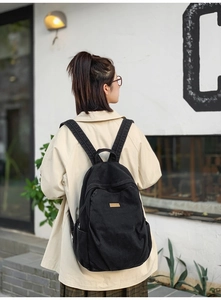 Detail of a black denim backpack with adjustable straps and logo patch for daily travel