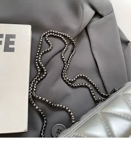 Detail of silver quilted crossbody bag with a dark gray metallic box chain texture