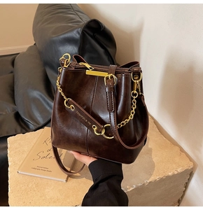 Detail of dark brown vintage bucket bag with wax leather texture and gold chain link strap