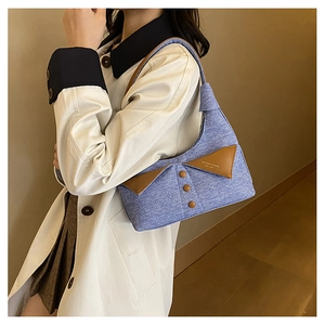 Détail du sac bandoulière en denim bleu avec rabat en cuir marron et boutons décoratifs