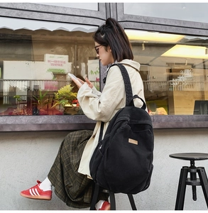 Detail of a large black canvas backpack featuring a brown leather patch logo on a street