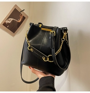 Detail of black matte leather bucket bag with chunky gold chain and metal tag