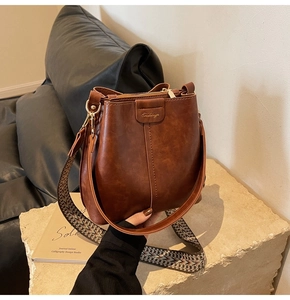 Close-up of deep brown leather bucket bag with jacquard strap on a stone pedestal