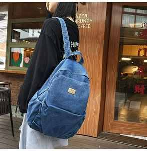 Outdoor shot showing a large blue denim backpack with a side pocket and leather logo