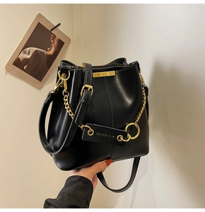Close-up of black leather bucket bag with gold chain strap and embossed leather tag