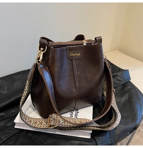 Detail of dark brown bucket bag with textured wide strap and golden logo on leather