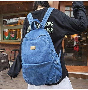 Detail of blue denim backpack showing wash texture and leather logo patch on pocket