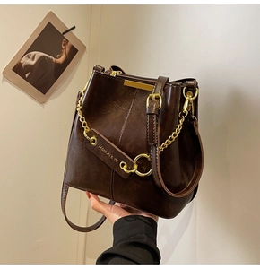 Close-up of vintage dark brown bucket bag with shiny leather texture and golden chain