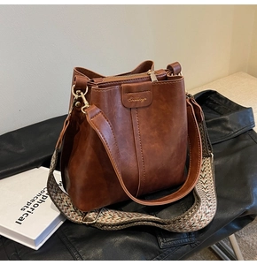 Close-up of brown bucket bag showing fine leather texture and colorful woven shoulder strap
