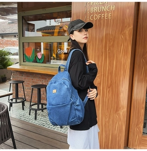Detail of blue denim backpack with leather logo patch and front zipper pocket