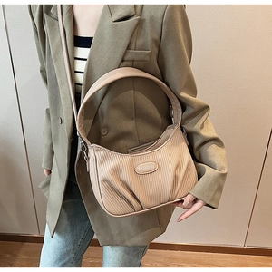 Detail view of beige pleated crossbody bag featuring a fashion emblem and textured leather