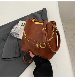 Close-up of vintage brown leather bucket bag with gold chain and debossed brand logo