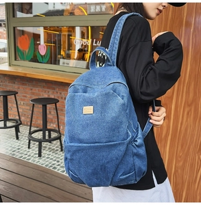 Outdoor street view of a blue washed denim backpack with brown patch and front zipper pocket