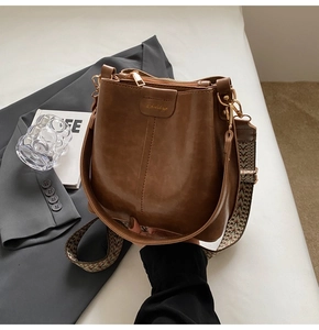 Close-up of brown leather bucket bag with retro woven shoulder strap and gold hardware