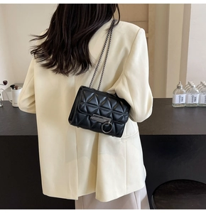 Detailed view of black quilted mini chain bag with metallic ring clasp on a model