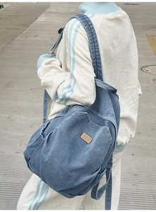 Outdoor shot showing the side profile of a large blue denim backpack on a model