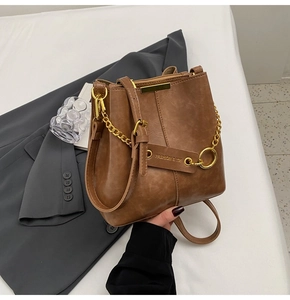 Detail of caramel bucket bag with gold chain and vintage leather texture on gray blazer