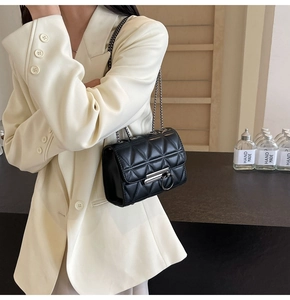 Detail of black quilted chain bag with silver ring clasp worn on white blazer
