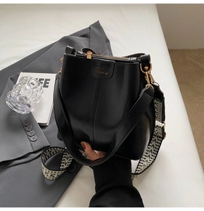 Detail view of black leather bucket bag with wide geometric strap and golden logo
