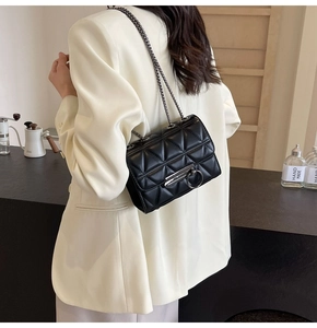 Detail of black quilted chain bag with silver buckle worn on a white blazer