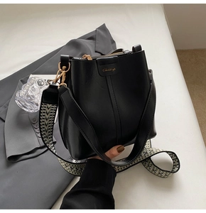Detail of black leather bucket bag with geometric strap and gold logo against a grey suit