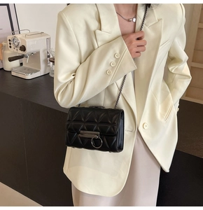 Detail of black quilted crossbody bag featuring a round metal lock and delicate chain strap