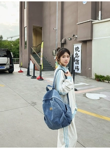Detail of blue denim backpack with pockets shown in a stylish outdoor street fashion setting
