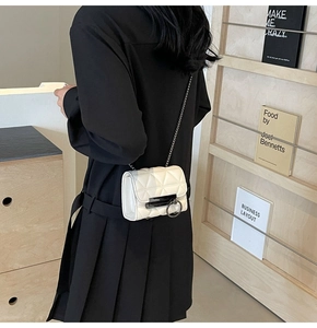 Detail of white quilted chain bag with round metal buckle worn by a model