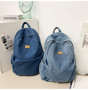 Detail view of two washed denim backpacks in deep and light blue with leather patch