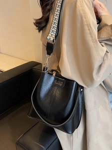 Sac seau chic en cuir noir avec bandoulière géométrique et finitions dorées sur mannequin