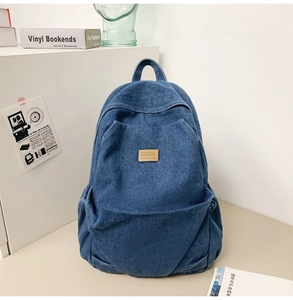 Detail of blue denim backpack showing brown leather logo and spacious front pocket