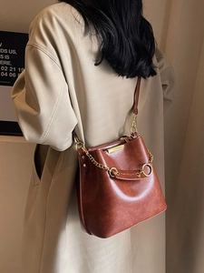 Brown vintage leather bucket bag with gold chain strap shown on a model in trench coat