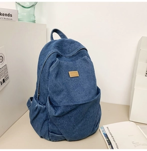 Detail of blue denim backpack showing textured fabric, leather logo, and front pocket