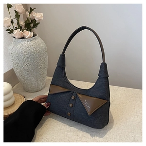 Détail d'un sac à main en jean avec col en cuir marron posé sur une table blanche