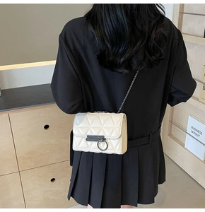 Detail of white quilted crossbody bag with metal ring buckle and chain strap on a person