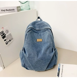 Detailed view of blue denim backpack with brown leather patch and side pockets texture