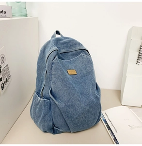 Detail of blue denim backpack showing brown leather patch and side pocket storage