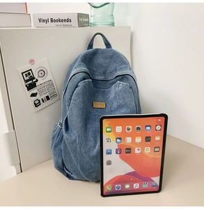Detail of blue denim backpack showing washed fabric texture and large capacity with a tablet