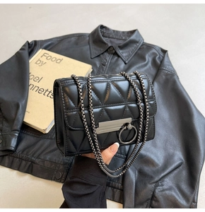 Detail of black quilted chain bag featuring a silver metal circular lock and leather texture