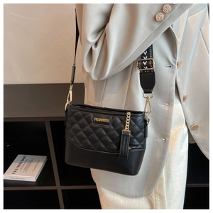 Détail du sac seau noir matelassé avec logo doré et large bandoulière à motif élégant