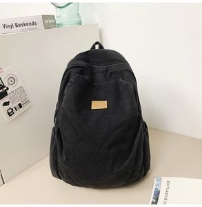 Detail of black canvas backpack with side pocket and logo patch in casual setting