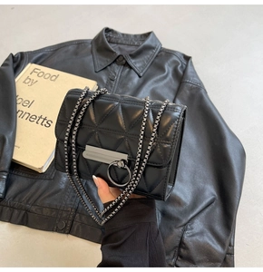 Detail of black quilted chain bag with rectangular hardware on a leather jacket